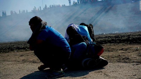 Migrants huddle to escape the effects of tear gas released by US troops on the Mexican border. Photo: Ramon Espinosa / AP