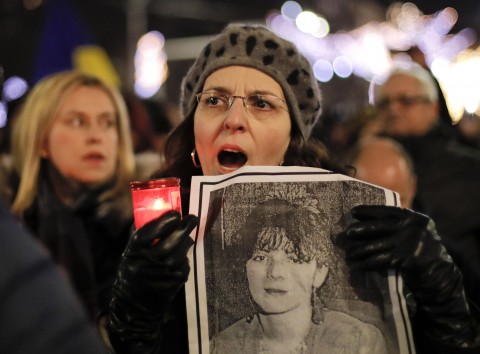 A woman holds a photograph of a 1989 uprising victim while singing the national anthem along with others during a protest in Bucharest on Saturday. More than 1,000 Romanians have demanded more democracy. Photo: AP
