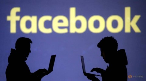 Silhouettes of laptop users are seen next to a screen projection of Facebook logo in this picture illustration taken March 28, 2018. 
