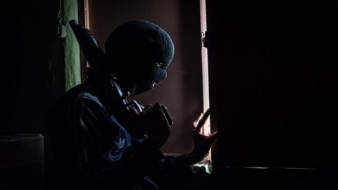 A member of a kidnapping gang watches through the window to avoid a potential police raid. He is 15 years old and joined the gang to support his family.