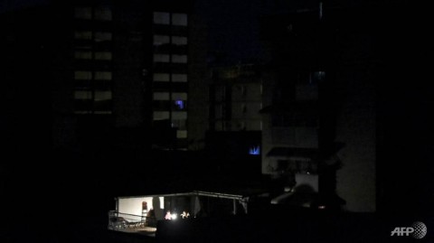 People sit around a light lamp outside their house during a power outage in Caracas.