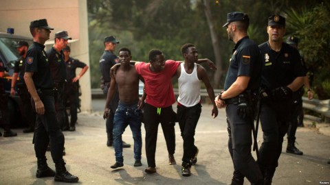 Police stand around a group of African migrants after they crossed the border fence from Morocco to Spain's North African enclave of Ceuta, Spain, Aug. 7, 2017. Photo: Reuters