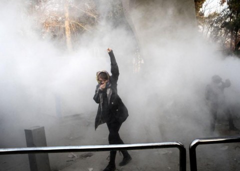 An Iranian woman raises her fist amid the smoke of tear gas during a protest at the University of Tehran on December 30, 2017. STR/AFP/Getty Images