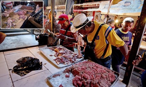 Desperate: A customer smells a piece of spoiled meat at a market in Maracaibo, where locals are lining up to buy rotten beef despite the health risk. Photo: AP