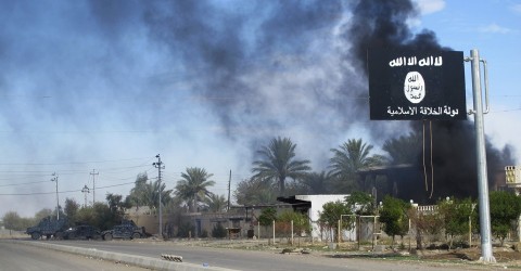 Smoke rises behind an Islamic State flag in Syria in 2014. Photo: Stringer Iraq / Reuters