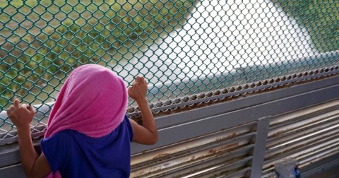 Genesis, a five-year-old from Honduras, peers through fencing in June along a bridge connecting Brownsville, Texas, and Matamoros, Mexico. Photo: Miguel Roberts/AP
